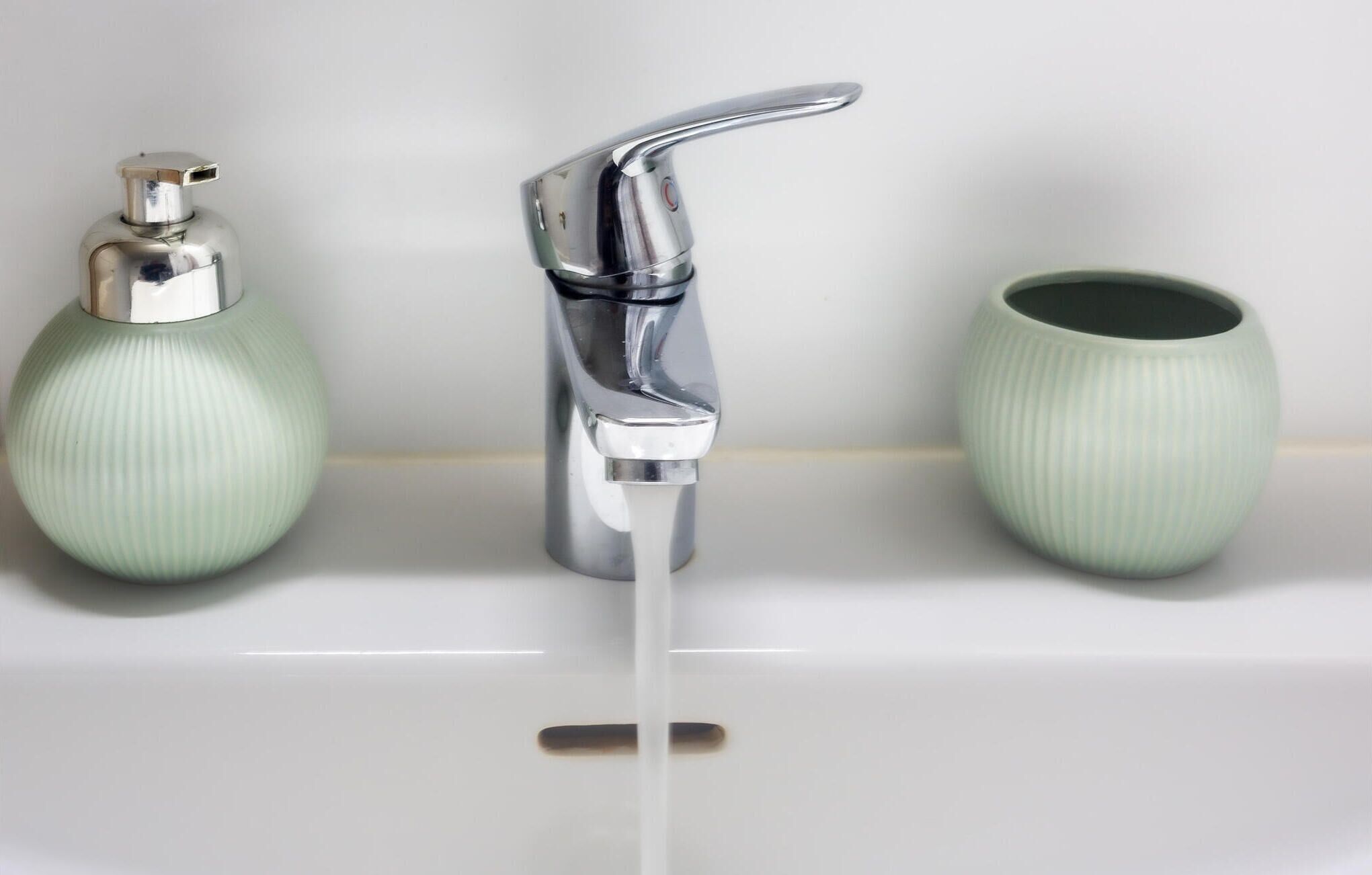 Un bagno con un rubinetto cromato, una vasetta verde e un’altra vasetta verde coordinata su un lavandino bianco.