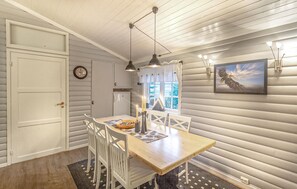 A dining area with a wooden table, white chairs, pendant lights, a window with curtains, a clock, and a framed picture on the wall. - 3 bedroom nice home in Leknes (Leknes)