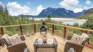 Una terraza con mobiliario de mimbre, una mesa de vidrio y una chimenea de piedra.