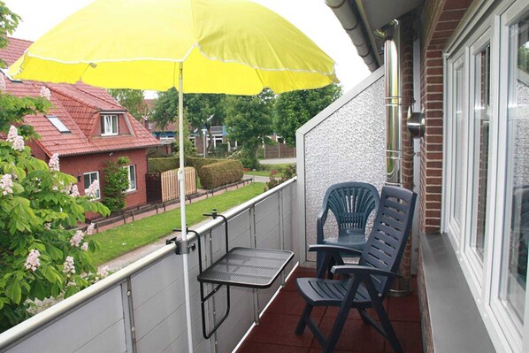 Un balcon avec un parasol jaune, deux chaises et une petite table.