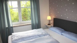 Un dormitorio con cama, mesita de noche, lámpara y ventana con cortinas.
