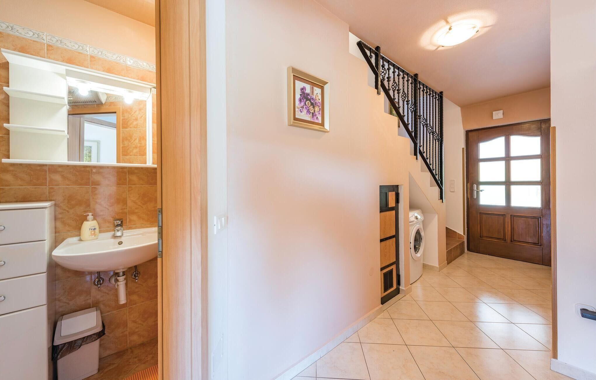 A hallway with a bathroom on the left, a staircase with a black railing, and a wooden door with glass panels on the right.