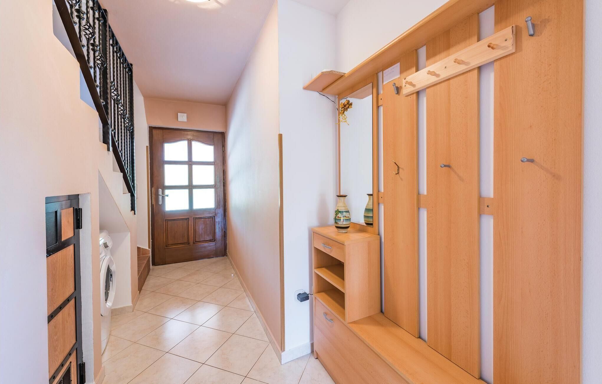 A hallway with a wooden wardrobe, a small table with a vase, and a staircase with a metal railing.