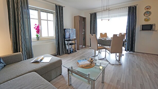 A modern living room with a sofa, a glass coffee table, a television, and a dining area with chairs and a table. - Apartment Albatros - Holiday home Goethestraße, Apartment Albatros (Apt. 18) (Heringsdorf)