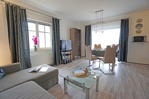 Un salon moderne comprenant un canapé, une table basse en verre, un téléviseur et un coin repas avec des chaises et une table.