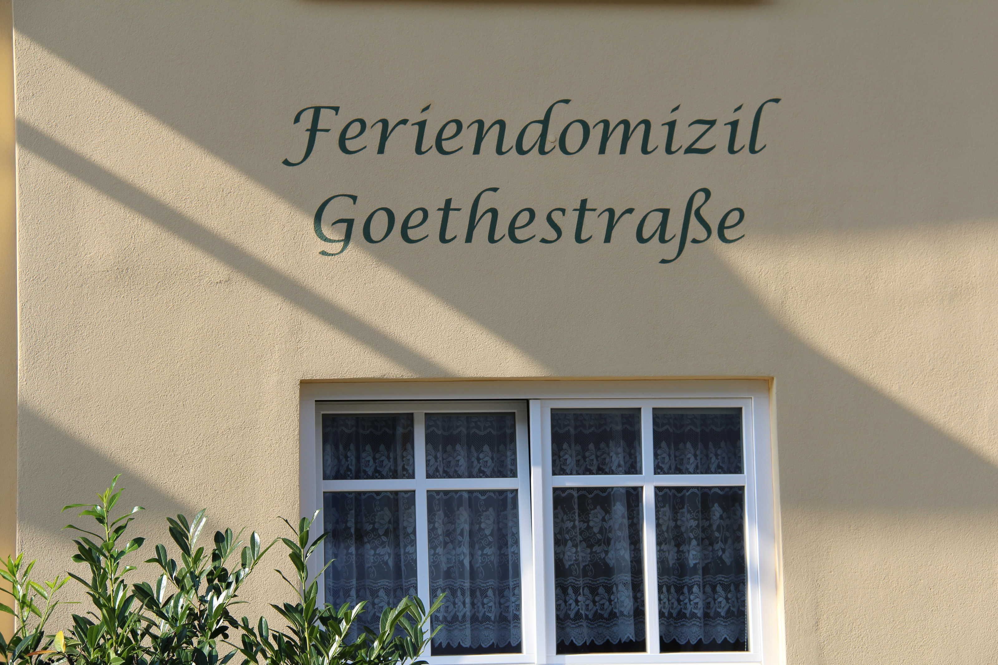 A building with the sign "Feriendomizil Goethestraße" above a window with lace curtains.