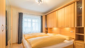 A bedroom with a double bed, wooden wardrobe, and a window with curtains. - Apartment Albatros - Holiday home Goethestraße, Apartment Albatros (Apt. 18) (Heringsdorf)
