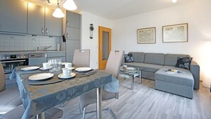 A modern kitchen with grey cabinets, a dining table set with plates and glasses, and a grey sofa in the living area. - Apartment Albatros - Holiday home Goethestraße, Apartment Albatros (Apt. 18) (Heringsdorf)