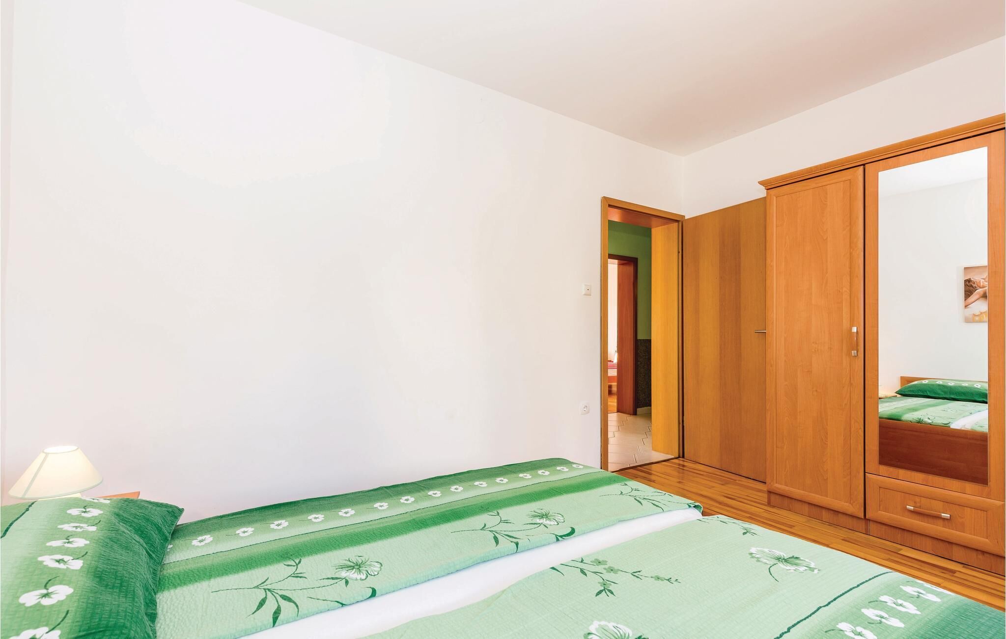 A bedroom with a bed, a wooden wardrobe, and a green floral bedspread.