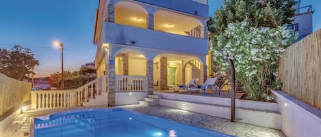 A two-story building with a swimming pool, outdoor seating, and a staircase leading to the upper level.