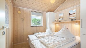 A wooden-paneled bedroom with a bed, a window, and a wall-mounted shelf with pictures.