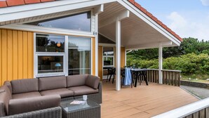 A covered outdoor area with a wooden deck, a brown sofa, and a glass table.