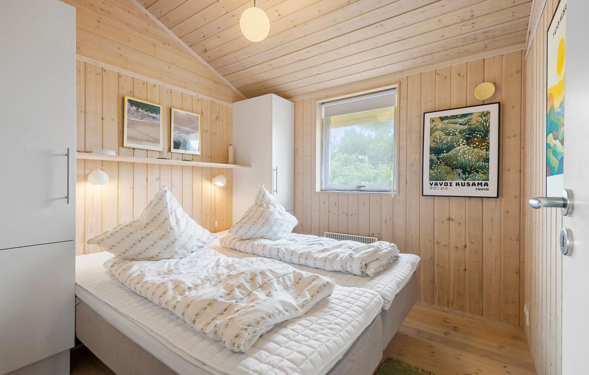 Een slaapkamer met twee bedden, houten wanden, een raam en een poster aan de muur.
