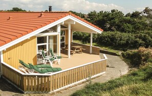 Relax on the covered porch with two lounge chairs and a picnic table amidst lush greenery and trees.