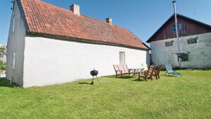 A white building with a red-tiled roof, a wooden table, and chairs in the yard.