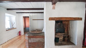 A rustic room with a brick fireplace, wooden beams, and a small window with a plant.