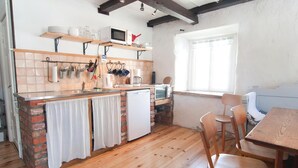 A compact kitchen with a brick backsplash, wooden counter, and a small refrigerator. There are hanging utensils and a microwave on the counter.
