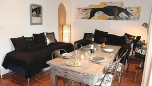 A dining area with a wooden table set for four, surrounded by black upholstered sofas. A painting of a whale hangs above the table. - Cozy home in Reillanne with WiFi (Reillanne)