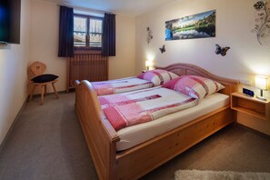 Un dormitorio con cama de madera, una silla, una mesita de noche con lámpara, una ventana con cortinas y adornos en la pared.