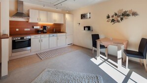 A compact kitchen with modern appliances, a dining area with two chairs, and a decorative wall piece. - Apartment 7 - Apartments Lohbinder (Fam. Holzer) (Rottach-Egern)