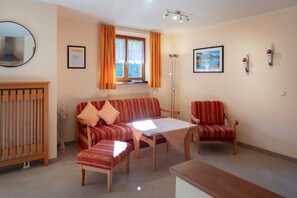 A living room with a sofa, two armchairs, a coffee table, a wooden bench, a mirror, a window with curtains, a floor lamp, and two framed pictures on the wall. - Apartment 7 - Apartments Lohbinder (Fam. Holzer) (Rottach-Egern)