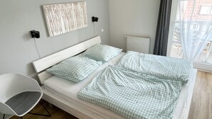 A modern bedroom with a bed, a chair, and a window with curtains. - Barbarossa Whg B-12. - B-12 (Kühlungsborn)