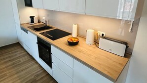 A modern kitchen with white cabinets, a black countertop, a sink, a coffee maker, a kettle, and a toaster. - Barbarossa Whg B-12. - B-12 (Kühlungsborn)