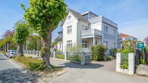 A two-story house with a balcony, a driveway, and a street with parked cars. - Barbarossa Whg B-12. - B-12 (Kühlungsborn)