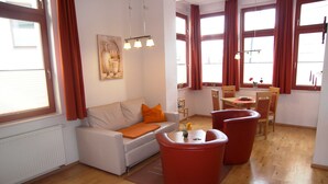 A modern living room with a sofa, red ottomans, a dining area with a table and chairs, and large windows with curtains. - Apartment 9 - Villa Meerblick - Ledwig, Villa Sea view (Heringsdorf)