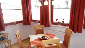 A dining area with a table set for four, wooden chairs, a small table with a tray, and a window with curtains. - Apartment 9 - Villa Meerblick - Ledwig, Villa Sea view (Heringsdorf)