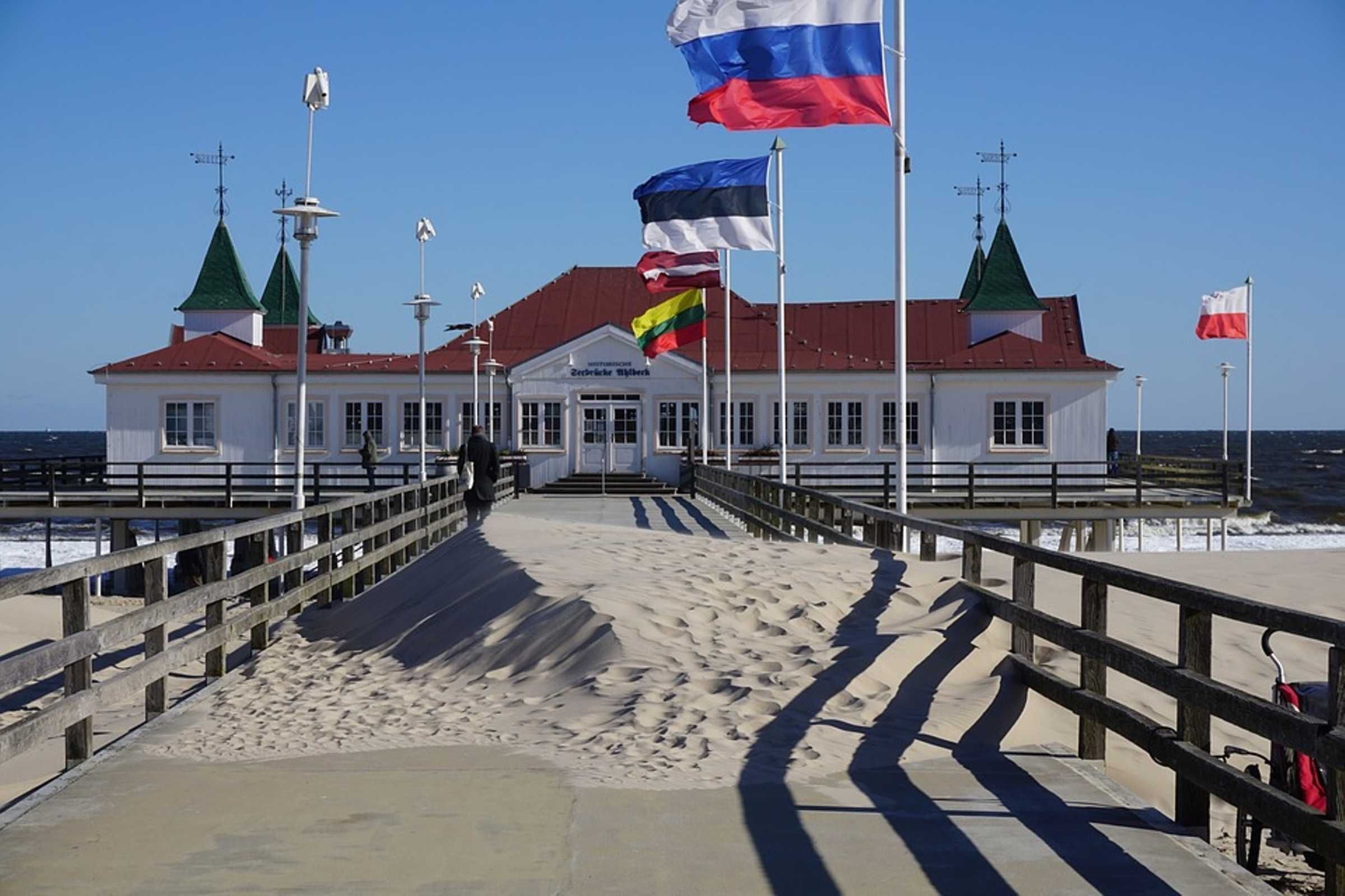 Een gebouw aan de kust met meerdere vlaggen, een zandstrand en een houten looppad naar de ingang.