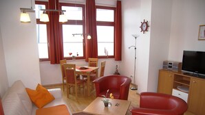 A living room with a sofa, two red chairs, a dining table with chairs, a TV, and a clock on the wall. - Apartment 9 - Villa Meerblick - Ledwig, Villa Sea view (Heringsdorf)