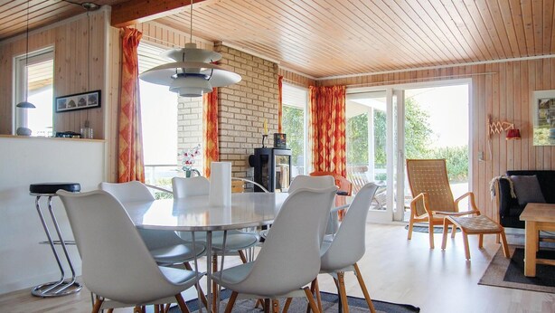 A modern interior with a round dining table surrounded by white chairs, a brick wall, and a large sliding glass door leading to an outdoor area. - Amazing home in Hejls with kitchen (Hejls)
