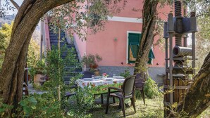 An outdoor dining area with a table set for two, surrounded by greenery and a pink building in the background. - Lovely home in Moneglia GE with WiFi (Moneglia GE)