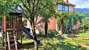 A residential backyard with a wooden play structure, a slide, a swing set, and a staircase leading to a house with a tiled roof. - Lovely apartment in Matulji (Matulji)
