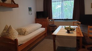 Ein gemütliches Zimmer mit einem Holzbett, einem kleinen Tisch mit einer Vase, einem Fernseher auf einer Holzkommode und einem Fenster mit Vorhängen.