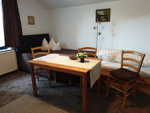 A small, cozy room with a wooden table, two chairs, a sofa, and a radiator. - Multi-bed room - Ferienhof Sarodnick (Lauta)