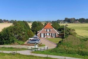A traditional brick house with a red roof, surrounded by a grassy field and trees.