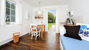 Una habitación luminosa con suelo de madera, una mesa de comedor con sillas, un sofá azul y vistas a un jardín a través de una puerta abierta.