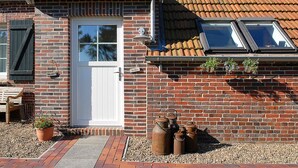 Una casa de ladrillo con una puerta blanca, un pequeño porche con un banco y una ventana con marco de metal.
