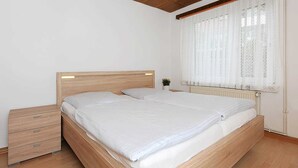 A bedroom with a wooden bed, a nightstand, and a window with sheer curtains. - Steering Wheel 2 - Apartments House Steering Wheel (Esens)