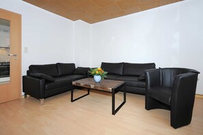 A modern living room with a black leather sofa set, a wooden coffee table, and a vase with flowers.