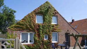 A house with ivy-covered walls, a wooden gate, and a patio with a table and chairs. - Steering Wheel 2 - Apartments House Steering Wheel (Esens)