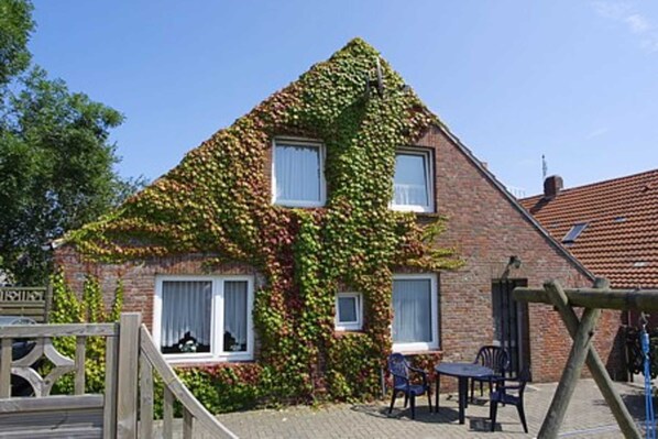 A house with ivy-covered walls, a wooden gate, and a patio with a table and chairs.