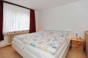 A bedroom with a bed, a bedside table, a window with curtains, and a radiator.