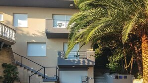 Un immeuble à plusieurs étages, doté d’un escalier menant à un balcon, le tout entouré de palmiers.