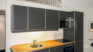 Una cocina moderna con armarios oscuros, encimera de madera, fregadero de acero inoxidable y horno empotrado.