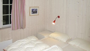 Un dormitorio con cama, mesita de noche, lámpara, ventana con cortinas y un cuadro en la pared.