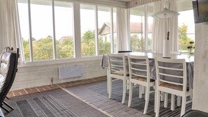 A sunroom with a table and chairs, large windows, and a view of trees and buildings outside. - 3 bedroom awesome home in Faaborg (Faaborg)