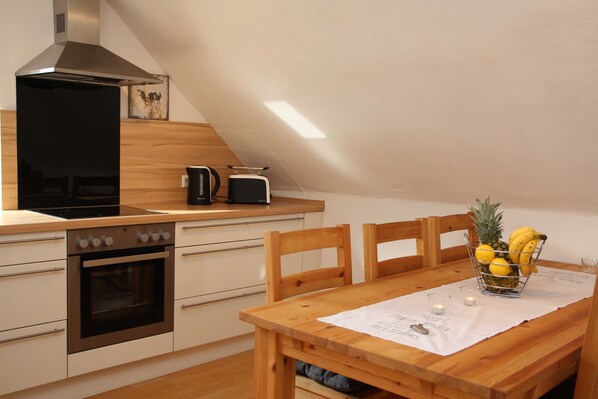 Une cuisine équipée d’une cuisinière, d’un four et d’un grille-pain sur le plan de travail. On y trouve également une table à manger avec des chaises et un panier de fruits.